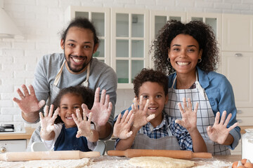 Head shot portrait happy African American family cooking baking together, smiling young mother and father with little son and daughter looking at camera, showing hands in flour, rolling dough