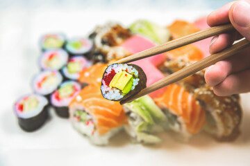 Man takes Tasty Colorful assorted Set of different type Sushi with chopsticks. Dinner in Japanese style. Healthy food. Filadelfia and Maki sushi rolls with Avocado, Tuna, Salmon, fish and Prawns.