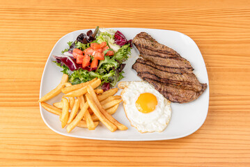 Combination dish with beef fillet, fried egg with yolk for dipping, French fries and salad of lettuce shoots and chopped tomato