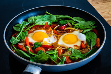Shakshuka - fried eggs with sausages and vegetables in frying pan
