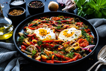 Shakshuka - fried eggs with vegetables on black wooden table
