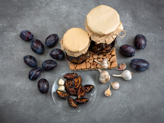 Home preparations for the winter. Jars with dried plums and garlic in oil. Autumn preparations. Healthy diet. View from above. Gray background.