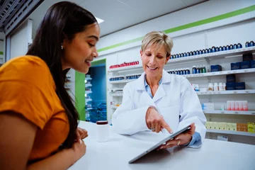 Foto op Canvas Caucasian pharmacist scrolling on digital tablet reviewing cold and flu medication to mixed race patient standing in pharmacy  © Prins Productions