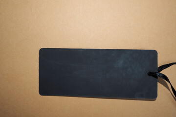 a black rectangular clothing tag with a black thread lies on a brown background. top view