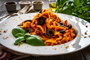 Fettuccine and chicken nuggets with tomato and basil sauce with black  olives on wooden table