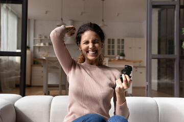 Fototapeta na wymiar Excited young Caucasian woman have fun play video games online at home. Happy millennial female sit relax on sofa in living room engaged in funny playful gaming activity. Entertainment concept.