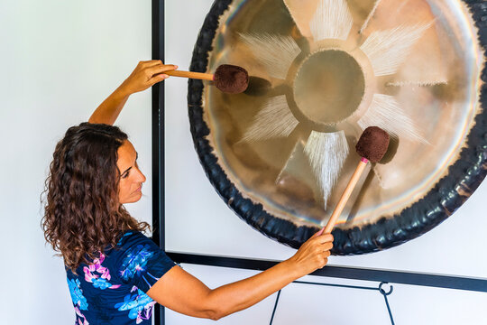Female sound therapist playing gong with mallets in studio