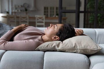 Fototapeta premium Tired calm millennial Caucasian woman lying relaxing on couch at home sleep or take nap. Exhausted asleep young female renter rest on comfortable sofa furniture daydream on pillow. Fatigue concept.