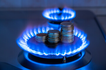 Fototapeta Gas stove lit, with stacks of coins above it. Increase in gas costs and tariffs.
 obraz
