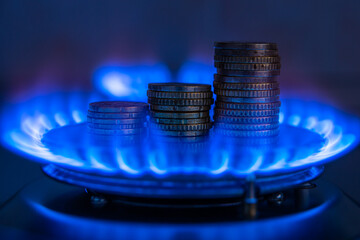 Gas stove lit, with stacks of coins above it. Increase in gas costs and tariffs.
