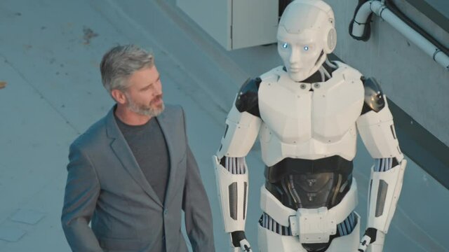 Caucasian business leader adult talking with robotic cyborg, explaining future project ideas and collaborating. Human and robot on rooftop. Innovation, career and technology.