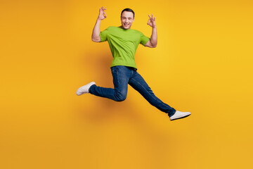 Fototapeta na wymiar Portrait of sportive excited guy jump raise hand show okey on yellow wall