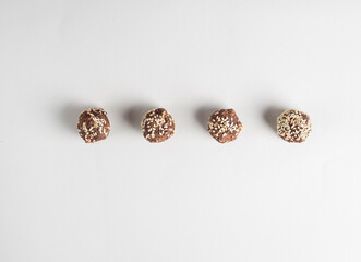 Brown vegetarian candies (energy balls) decorated with cocoa and sesame seeds lie in a row one after another. Raw food sweets. Gray background. Proper nutrition. View from above. Flat lay.