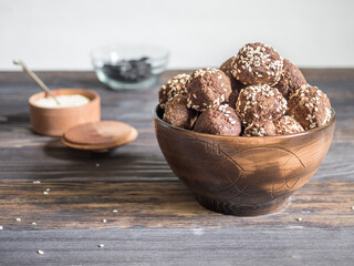 Brown.vegetarian sweets decorated with sesame seeds and carob powder in a ceramic bowl on the table along with the ingredients. Energy balls.  Raw food sweets. Proper nutrition.