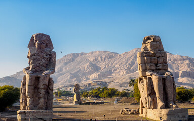 Two ancient Pharaoh statues inside Luxor in a blur background of mountain 
