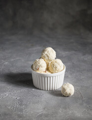 White sugar free vegetarian sweets garnished with coconut flakes in a white ceramic bowl on a gray background. Raw food sweets. Energy balls.  Proper nutrition. Vegan snack. Copy space