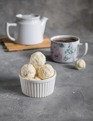 White Sugar-free vegetarian sweets garnished with coconut flakes in a white ceramic bowl on a gray background with a mug of tea. Tea drinking. Energy balls.  Raw food sweets. Vegan snack