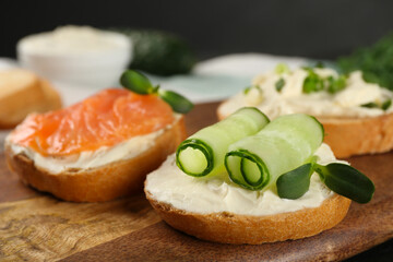 Delicious sandwiches with cream cheese and other ingredients on wooden board, closeup