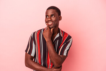 Young African American man isolated on pink background relaxed thinking about something looking at a copy space.