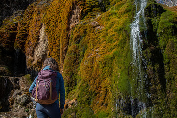 A hiker in front of the colorful waterfall in Dreimühlen