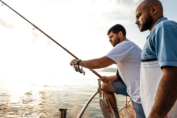 Two young men standing on sailboat with fishing rod looking at haul