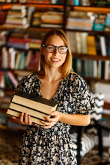 Back to school library concept. Student girl holding book on her hands on background of bookshelves...