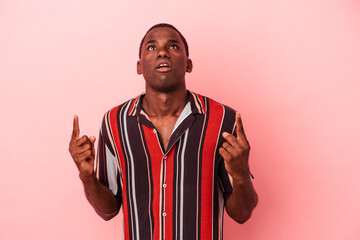 Young African American man isolated on pink background pointing upside with opened mouth.