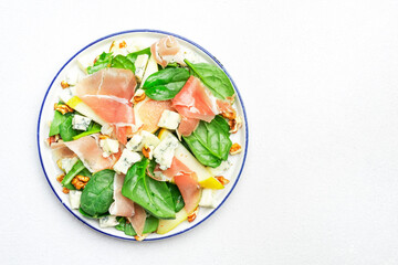Pear salad with prosciutto, blue cheese, spinach, walnuts on white background, top view, copy space