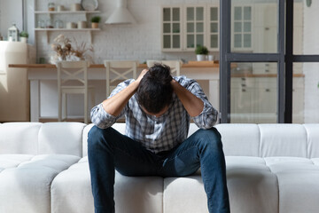 Depressed African American man thinking about personal problems, sitting on couch at home alone,...