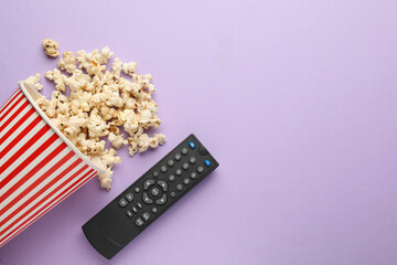 Remote control and cup of popcorn on violet background, flat lay. Space for text