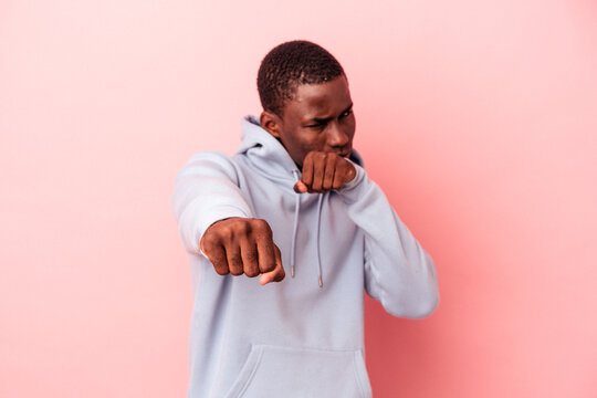 Young African American man isolated on pink background throwing a punch, anger, fighting due to an argument, boxing.