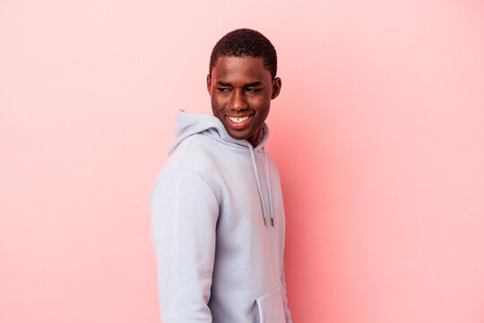 Young African American man isolated on pink background looks aside smiling, cheerful and pleasant.