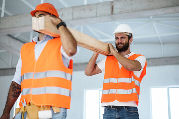 Two young men builders carrying wood planks on construction site, close up