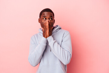 Young African American man isolated on pink background thoughtful looking to a copy space covering mouth with hand.