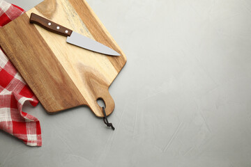 Wooden cutting board, knife and kitchen towel on light grey table, flat lay. Cooking utensils