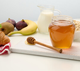 honey in a glass transparent jar and a wooden stick on a white table