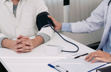 Asian doctor is using a patient's blood pressure monitor at the time of his annual check-up and explains his blood pressure.