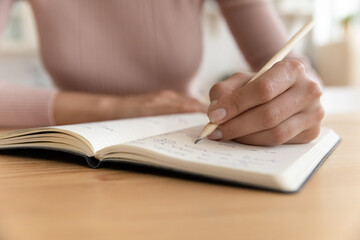 Crop close up of female student make note handwrite in notebook studying at home. Caucasian woman write in notepad, make list or plan, engaged in time management activity. Education concept.