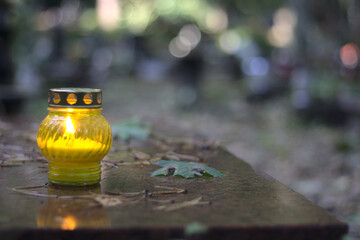 A yellow candle (snitch) on a tombstone, in a cemetery during the day. All Saints' Day, copy space.