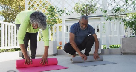Animation of happy african american senior couple rolling yoga mats on patio