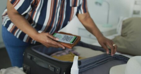 Animation of african american senior woman packing covid vaccine passport into suitcase - Powered by Adobe