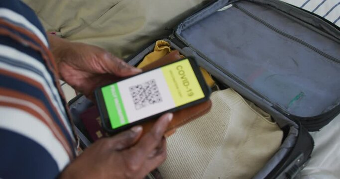Animation of hands of african american senior woman packing covid vaccinate passport into suitcase