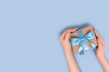 Female hands hold gift box on a blue background. Present tied with a ribbon. Festive composition with place for text.