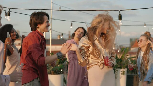 Multi ethnic friends drinking alcohol and dancing on rooftop