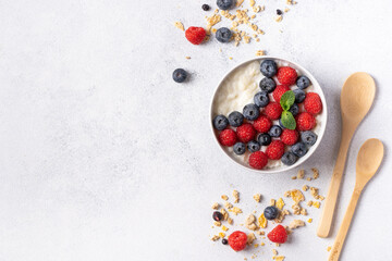 Homemade granola in a white plate with berries and fruits. A healthy breakfast, a source of protein and useful substances. Gray background, top view.