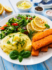 Fried fish sticks with potato puree and fresh vegetable salad on wooden table
