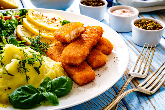 Fried fish sticks with potato puree and fresh vegetable salad on wooden table
