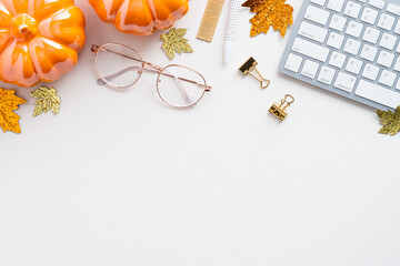 Autumn desk table with pumpkins, keyboard, glasses on white background. Blogger workspace top view. Flat lay. Cozy, hygge style workplace.