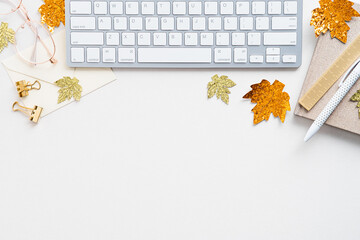 Autumn desk table with computer keyboard, maple leaves, notebook on white background. Flat lay, top...