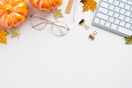 Autumn desk table with pumpkins, keyboard, glasses on white background. Blogger workspace top view. Flat lay. Cozy, hygge style workplace.